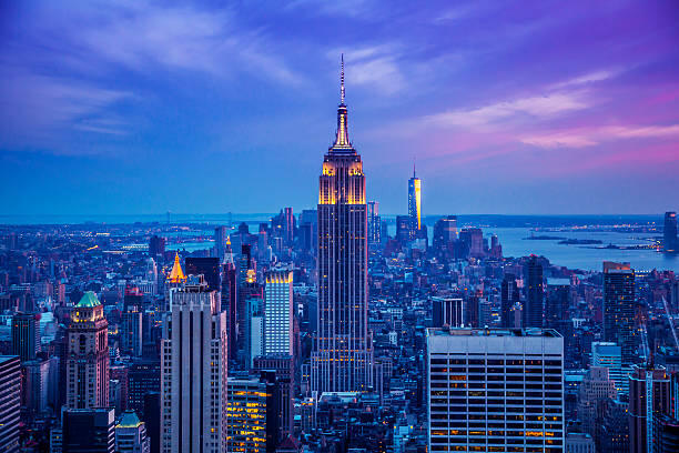 An image depicting an elevated perspective in New York City. From high up, you can see the Empire State Building behind another prominent building that I forgot the name of. The entire image has a general color scheme of blue, purple, and pink, as well as
